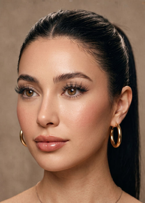A close-up portrait of a woman with dark hair in a ponytail, wearing Instant Glam wispy mermaid style self adhesive lash clusters.